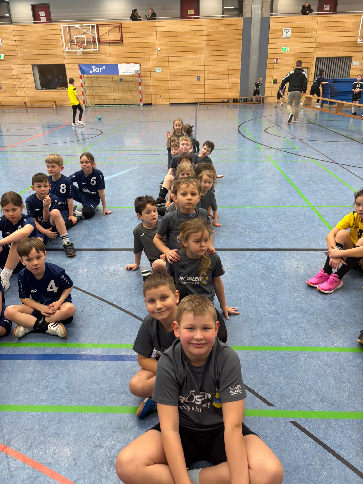 Die Handballjugend sitzt aufgereiht in der Halle und wartet konzentriert